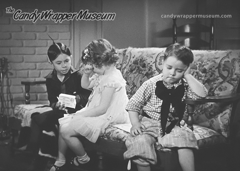 Three children sitting on a couch. Spanky looking dejected as Alfalfa tries to win the love of Marianne.